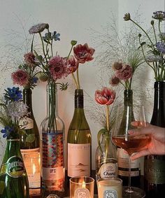 a table topped with lots of bottles and glasses filled with wine next to candles on top of a wooden table