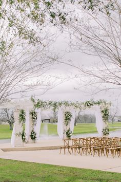 an outdoor wedding setup with white draping and flowers on the arbors, set up for a ceremony