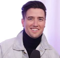 a man is smiling and holding a microphone in front of him, while wearing a gray jacket