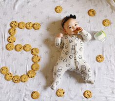 a baby laying on top of a bed next to cookies