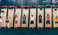 a group of people standing next to each other in front of a wall holding up their hands