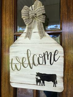 a welcome sign hanging on the front door with a cow and calf painted on it