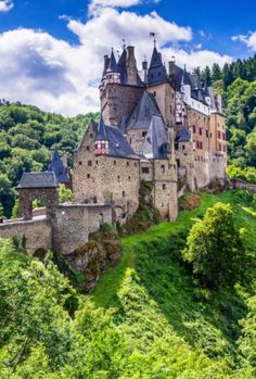 an old castle on top of a hill surrounded by trees and greenery under a blue sky with clouds