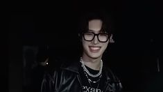 a young man wearing glasses and a black leather jacket is smiling at the camera in the dark