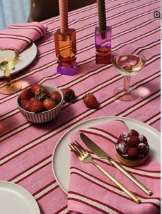 the table is set with pink and white striped linens, goldware, strawberries, candles, and wine glasses