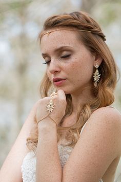 a woman with her hands on her chin wearing gold jewelry and holding her hand near her face