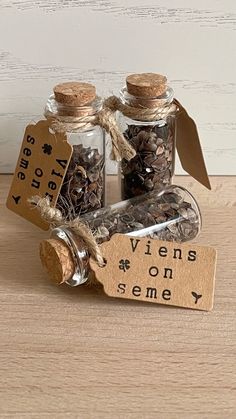 two small glass bottles filled with nuts on top of a wooden table next to a tag