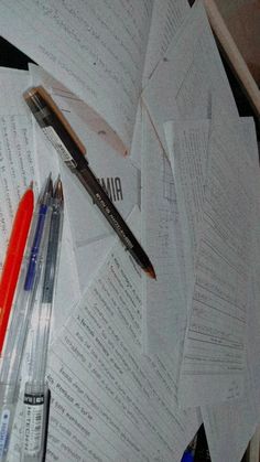 several papers and pens on top of each other with one pen laying on the paper