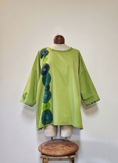 This tunic style top was made from a spring green 100% cotton sheet. It has handpainted happy flowers on it in shades of turquoise, teal and granny apple green. There's handstitchrd detail around the neckline and one of the sleeves. This top is super lightweight so it would be perfect for a hot summer day. She's a one size fits most.  The model generally wears a medium and is 5'9.  It would be oversized on a small and medium frame and fit nicely on a large. Handwashing or a delicate machine wash is recommended. Please let me know if you have any questions. Thank you! Spring Green Cotton Tunic, Hand Dyed Cotton Tops For Spring, Green Cotton Summer Tunic, Oversized Green Cotton Blouse, Relaxed Fit Blouse With Natural Dye For Spring, Relaxed Fit Green Cotton Blouse, Green Bohemian Cotton Top, Green Lagenlook Long Sleeve Blouse, Bohemian Green Cotton Top