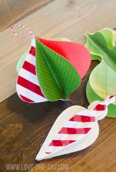 three paper christmas decorations on top of a wooden table with green leaves and red and white stripes