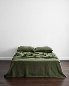 a bed with green linens and pillows in a white walled room next to a wooden floor