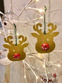 two reindeer ornaments hanging from a tree with lights on it's head and nose