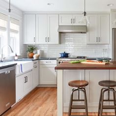 a kitchen with white cabinets and wooden counter tops, two stools in front of the island