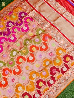 an orange and pink saree laying on top of green grass with colorful flowers in the middle