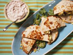 three quesadillas on a blue plate with a bowl of dip