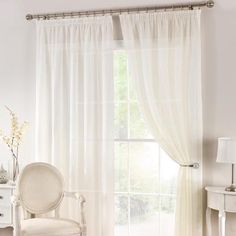 a white chair sitting in front of a window next to a table with flowers on it