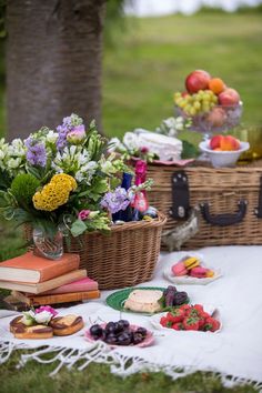 a picnic with fruit, flowers and books on the blanket in front of two wicker baskets