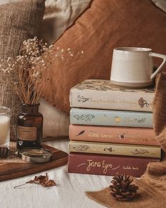 a stack of books sitting on top of a bed next to a cup and candle