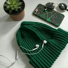 a green hat, sunglasses and headphones are sitting on a table next to a cell phone