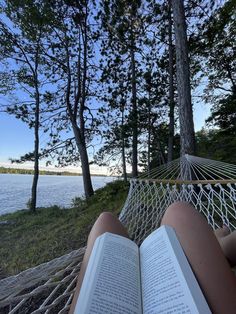 a person laying in a hammock reading a book by the water's edge