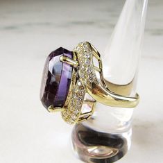 "This is an incredibly huge, vintage 18K amethyst & diamond ladies cocktail ring. The oval amethyst is a 17.1mm x 22.5mm created gemstone. It does have a few scratches. The 4 pronged setting is secure, but the stone does move a tad when wiggled. The ring face is accented with 60 round 1.5mm diamond gemstones. All 60 have a total carat weight of 1.2 carats. Two of the diamonds are cracked and their girdle is affected. The band is sized at a 9. The band is stamed 750 inside (18K). The entire r Luxury Oval Amethyst Collectible Ring, Exquisite Oval Amethyst Ring For Formal Occasions, Luxury Oval Amethyst Ring For Formal Occasions, Elegant Oval Amethyst Ring With Diamond Accents, Formal Purple Amethyst Ring With Rose Cut Diamonds, Formal Amethyst Ring With Rose Cut Diamonds, Luxury Oval Amethyst Ring With Diamond Accents, The Ring Face, Amethyst Gem