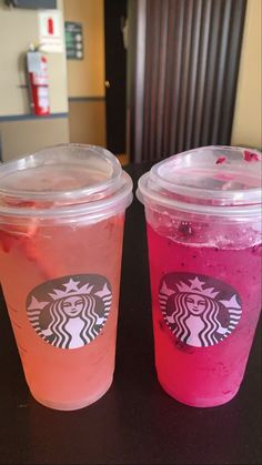 two starbucks drinks are sitting on a table with pink and red liquid in the cups