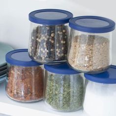 four glass jars filled with different types of spices on top of a white countertop