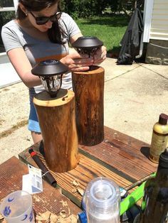 a woman standing next to two wooden cylinders on top of a picnic table in the sun