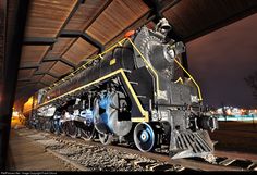 an old fashioned train is parked on the tracks in front of a covered area at night