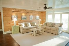 a large living room with wood paneling and white furniture in the middle of it