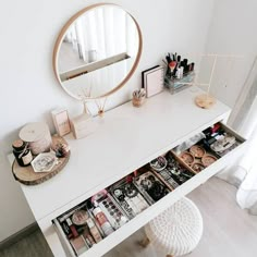 a white desk with drawers and makeup on it in front of a round mirror above the counter