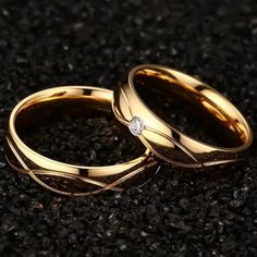 two gold wedding rings sitting on top of each other with a diamond in the middle