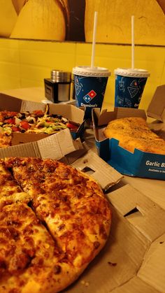 two pizzas and drinks are sitting on the table in front of some food items