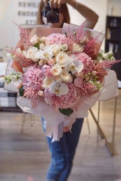 a woman holding a bouquet of pink and white flowers with a camera in her hand