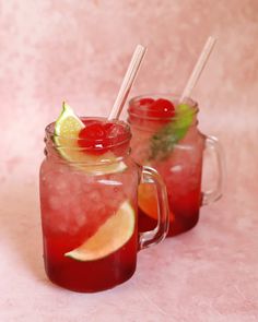 two mason jars filled with red liquid and garnished with lemon, lime and cherries