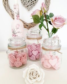 three jars filled with pink and white flowers next to a heart shaped wall hanging on the wall