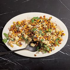 a white plate topped with lots of food on top of a black table next to a spoon