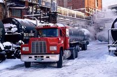 a red semi truck driving down a snow covered street next to train tracks and buildings