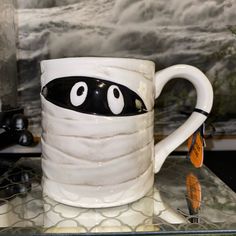 a white coffee mug with black eyes on it sitting on top of a glass table