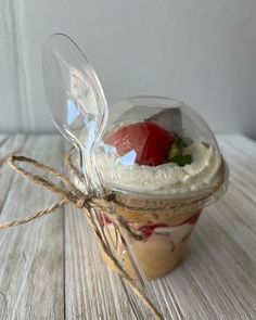 a glass jar filled with whipped cream and strawberries on top of a wooden table