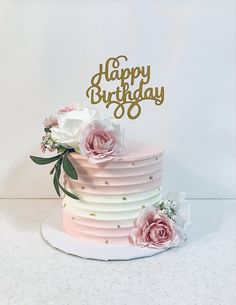 a three tiered cake with pink and white flowers on the top is decorated with gold lettering that says happy birthday