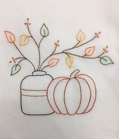 two pumpkins and a vase with leaves on it are embroidered onto a white cloth