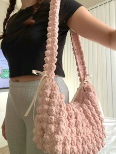 a woman holding a pink crocheted purse in front of her face and wearing leggings