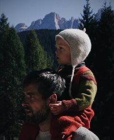 a man holding a small child on his shoulders in front of some trees and mountains