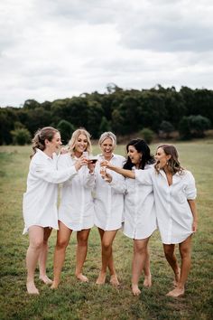 four women in white robes toasting with each other while standing on a grassy field