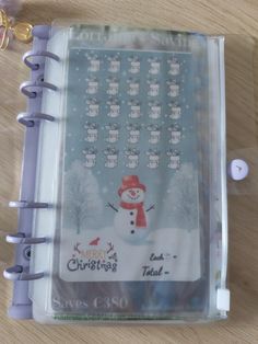 a christmas planner with a snowman on the front and numbers in the back, sitting on a wooden table