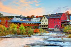 a river running through a lush green forest next to a tall red building with a bridge over it