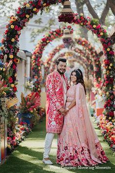 a man and woman standing in front of an archway with floral decorations on it, posing for the camera