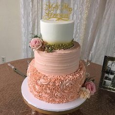 a three tiered cake with pink frosting and gold lettering on top is sitting on a table