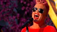 a woman with pink hair and sunglasses singing into a microphone